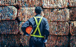 Employee wearing safety equipment stands in front of compressed bricks of recycled material.